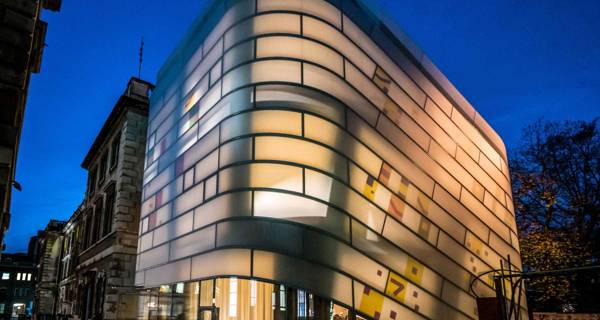 Exterior view of Maggie’s Cancer Care Centre at St Bartholomew’s Hospital, featuring its distinctive ‘lantern-like’ design with curving glass and concrete elements